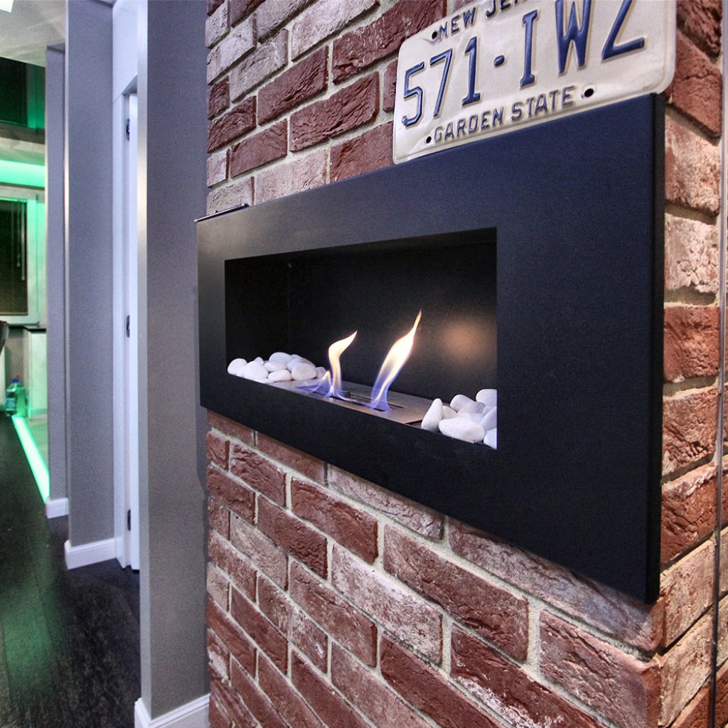 Ściana z czerwonej cegły z wpuszczonym w czarną płytę biokominkiem